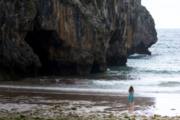 Alone girl walking in a beach with a cliff in the background. Location Sea caves beach in Asturias,...