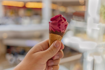 Close up of man hand holding fresh waffle cone with raspberry sorbet and chocolate.