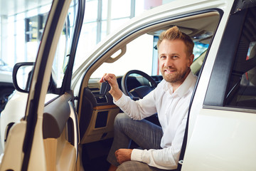 Naklejka premium Auto buyer man with keys in hand in a new car in auto salon.