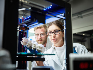 Two technicians looking at turbine wheel being printed in d printer