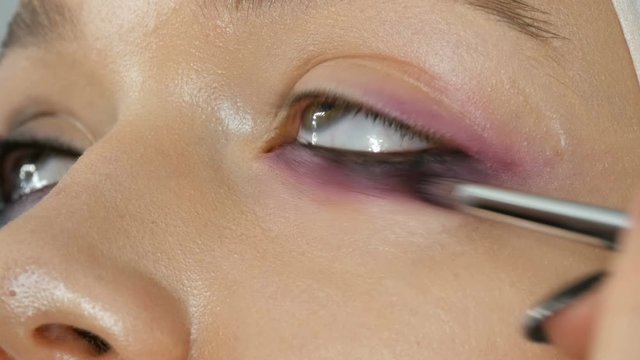 Woman make-up artist stylist makes makeup fashionable pink smoky eyes with special makeup brush of a young model