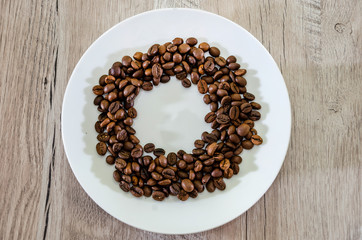 coffee beans in a white plate on a wooden table background. View from above.