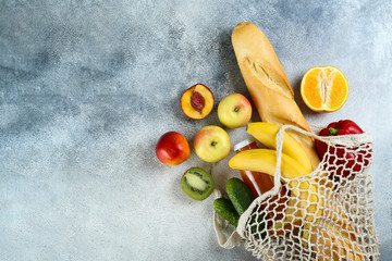 Bunch of mixed organic fruits, vegetables & greens, gourmet pile in full eco friendly shopping bag to reduce ecological footprint. Zero waste concept. Grunged stone background, copy space, close up.