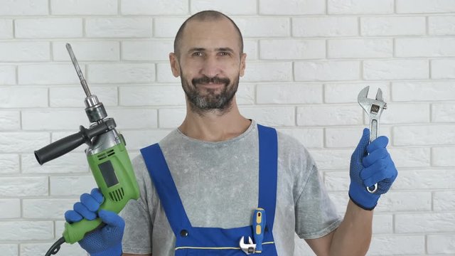 Builder with tools. Happy builder holds a drill in one hand and an adjustable wrench in the other.
