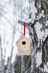 Wooden birdhouse on a branch of tree in winter snowy forest.
