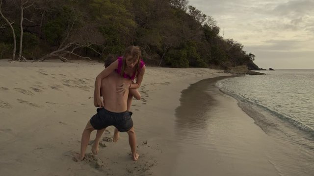 Slow motion tracking shot of man chasing woman on beach then dunking her in ocean / Anse La Roche bay, Carriacou, Grenada