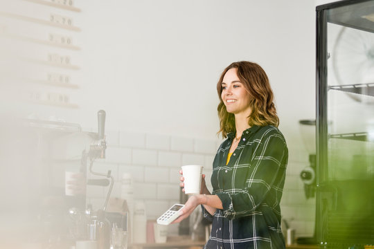 Young woman, working in coffeeshop, offering card reader