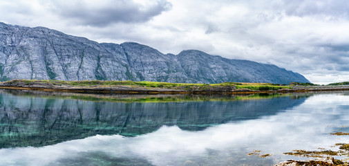 Panorama of clouds above fjord and mountains with green grass on the Alsta Island, close to Sandnessoen town Norway