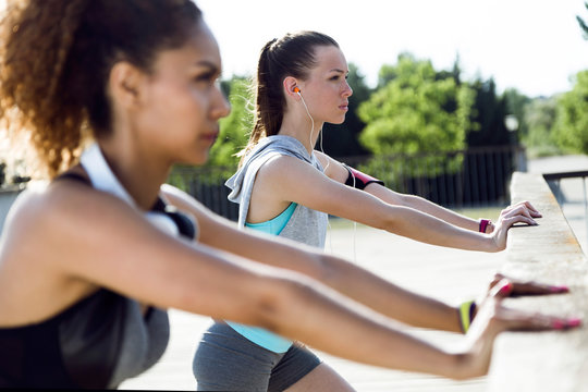 Two sporty young women stretching on bridge railing