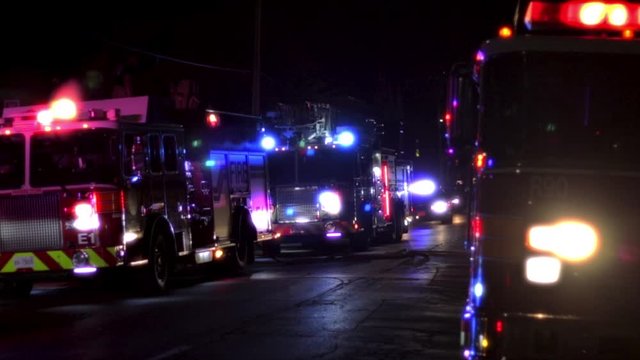 Firetrucks at night blocking off the street with bright flashing blue and red lights. 911 alarm conditions with fire engines on the street at night. Team of firemen on the scene of a fire. 