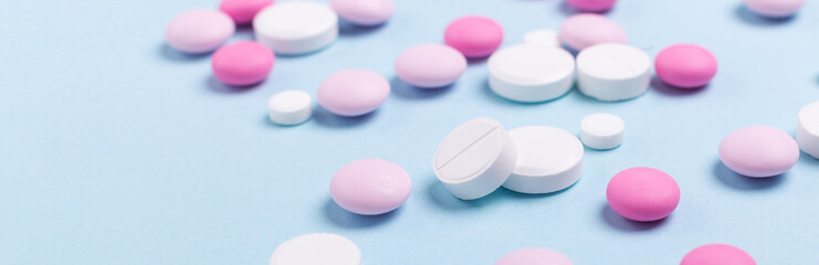 Obraz na płótnie Canvas Pink and white tablets on blue background Heap of assorted various medicine tablets Horizontal banner Health care Close-up Copy space