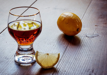 Brandy or cognac in the glass with lemon on table. Wooden table background texture. Brown strong alcohol drink for relaxation and nightclub.