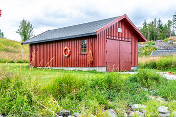 Typical fishermen's boathouse in Norway - classical red, wooden scandinavian small building. Green grass, close to coast. The Donna Island, Northern Norway
