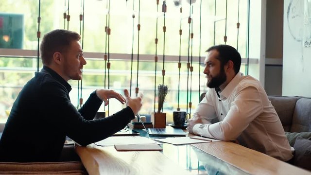 HR manager having job interview with young man in cafe and watching his resume application in laptop during coffee break. Confident businessman conducts interview with candidate for job in slow motion