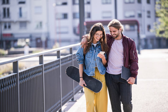 Young couple with skateboard and smartphone walking on a bridge
