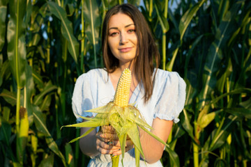 Brunette in a blue dress holding an ear of corn. Selective focus on corn