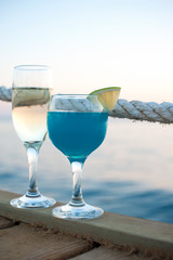 Two glasses with champagne and fresh blue cocktail at sunset