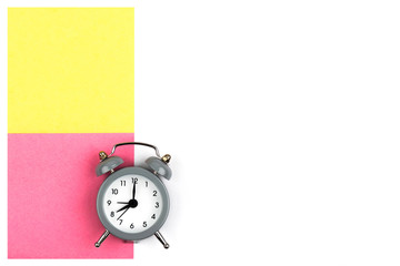 Clock with an alarm clock on a white background lie on colored paper leaves of pink и yellow color for notes