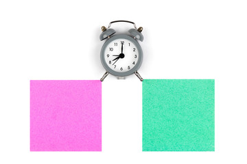Clock with an alarm clock on a white background lie on colored paper leaves of green and raspberry color for notes