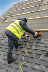 Workman using pneumatic nail gun install tile on roof of new house under construction