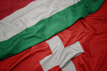 waving colorful flag of switzerland and national flag of hungary.