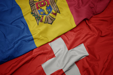 waving colorful flag of switzerland and national flag of moldova.