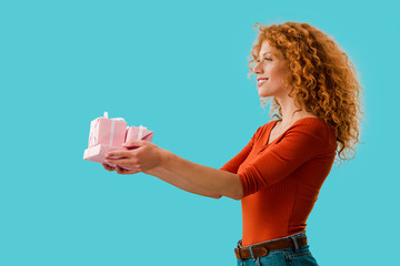 curly redhead woman holding gifts isolated on blue