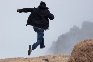 boy jumping off foggy moountain