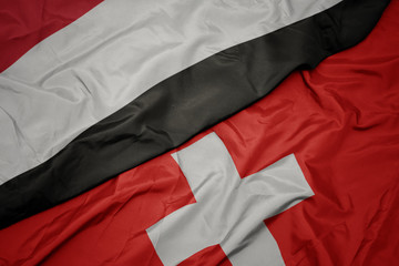 waving colorful flag of switzerland and national flag of yemen.