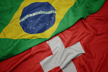 waving colorful flag of switzerland and national flag of brazil.