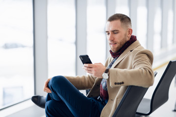 young busy man waiting for departure at the airport while using his phone