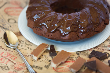 Round chocolate cake with chocolate topping on white plate with pieces of milk and bitter chocolate
