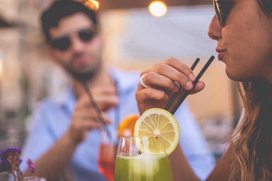 Young woman drinks cocktails at a table of friends. A boy with sunglasses blurred in the background. Friends having fun drinking alcohol at the bar. Filtered image