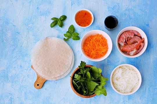 Ingredients for cooking spring rolls: sheets of rice paper, rice noodles, grated carrots, shrimps, salad mixture, soy sauce, chili sauce, basil. Top view. Vietnamese cuisine.