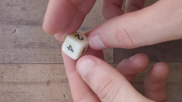 Hands examining a white 6 sided die, up close. 4k, flat lay, static, slow.