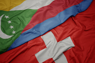 waving colorful flag of switzerland and national flag of comoros.