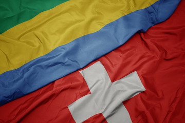waving colorful flag of switzerland and national flag of gabon.