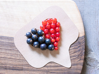 Black currant and red currant with leafs in wood jar and double colored heart  on wooden close up top view