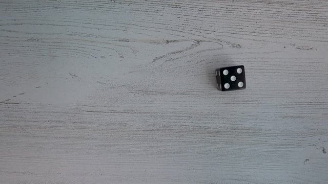 Six sided black die lands on a white wood table showing a 5, 4k flat lay.