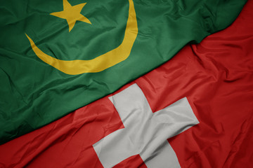 waving colorful flag of switzerland and national flag of mauritania.