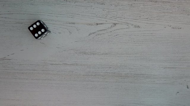 Rolling a 6 with a black six sides dice, 4k flat lay, above view, static.