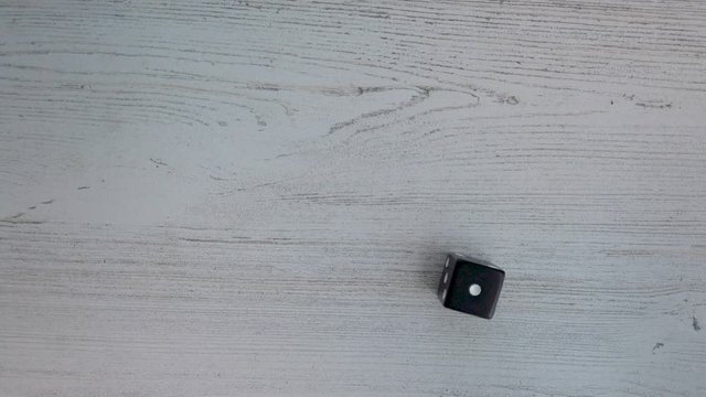 Hands shake a 6 sided die and roll a one. Single black die on white background.