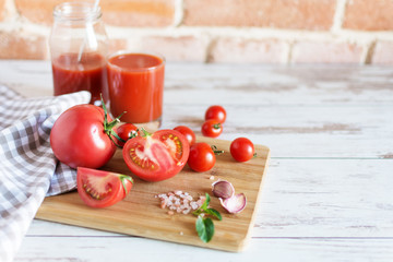Tomato juice in a glass and fresh tomatoes on wooden table. Salt and garlic for dressing.