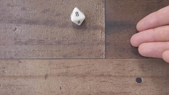 Hand showing an 8 sided die and rolls an 8, on isolated wood background flat lay