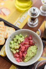 Raw tuna tartare with chopped cucumber and avocado guacamole in bowl on wooden board