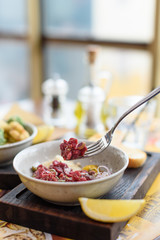 Beef tartare with capers, pistachios, onion, egg yolk and grated cheese in bowl on wooden board