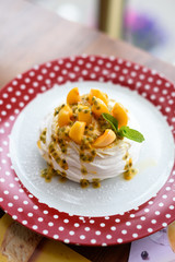 Mini Pavlova meringue cake with apricot and passion fruit on red polka dot plate, close up