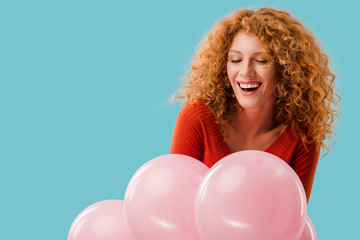 smiling redhead girl with pink balloons isolated on blue