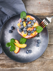 Juicy peach and blueberry dessert with cream close up top view on a dark plate