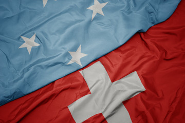 waving colorful flag of switzerland and national flag of Federated States of Micronesia .
